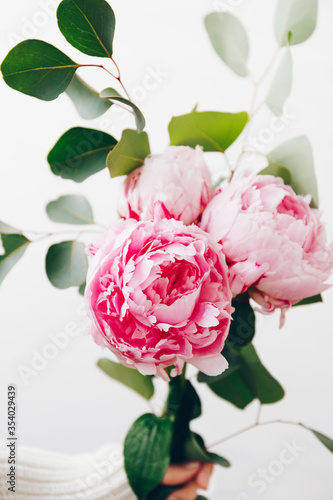 Girl s hand holds a beautiful bouquet with pink peony and eucalyptus branches.