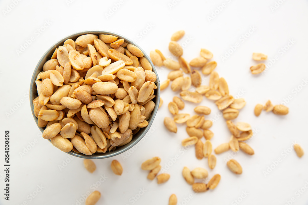 A pile of peanuts in a separate color cup on a white background top view