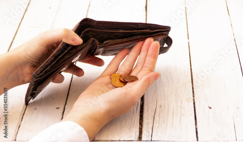 Man pouring coins into an empty wallet. Female hand holds an empty purse, coins in another hand, a trifle. Unemployment concept.
