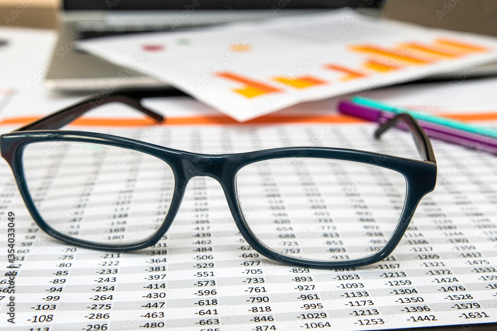 Detail of Numbered and graphic papers with glasses on them and a laptop Detail of Numbered and graphic papers with glasses on them and a laptop