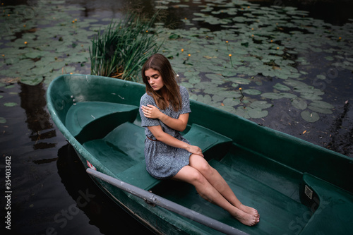 A young girl sits in an old boat against a background of water lilies