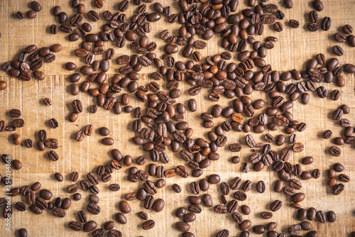 Roasted brown coffee beans spilled on wooden table background.
