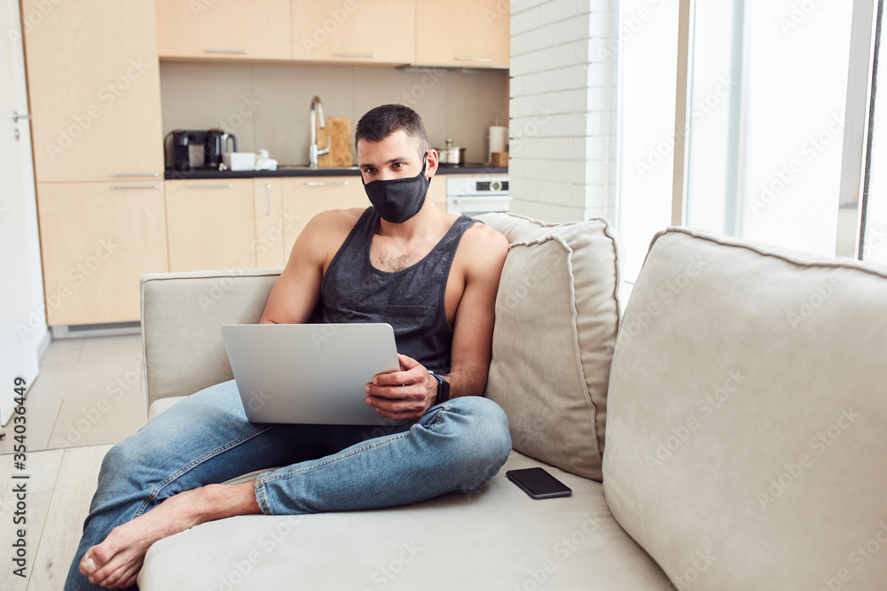 Handsome young man in medical face mask using laptop Handsome young man in medical face mask using laptop
