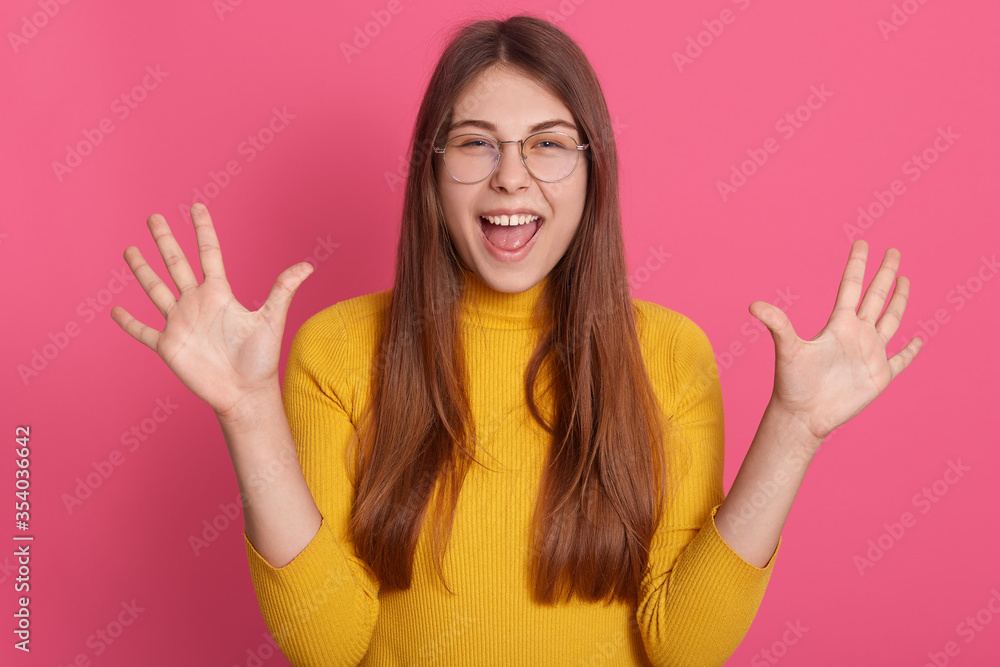 Portrait of happy excited female wearing yellow casual attire and glasses, raising palms up, expressing positive emotions, yelling something happily. Portrait of happy excited female wearing yellow casual attire and glasses, raising palms up, expressing positive emotions, yelling something happily.