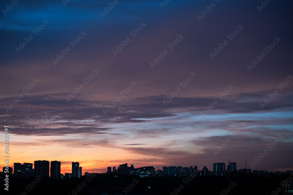 Warm sunset over city landscape with tall buildings and sky scrapers' silhouette in the foreground