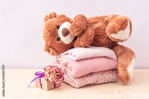 Teddy bear toy and Stack of knitted women's clothing, warm sweaters, a jacket, a blouse in pastel pink colors