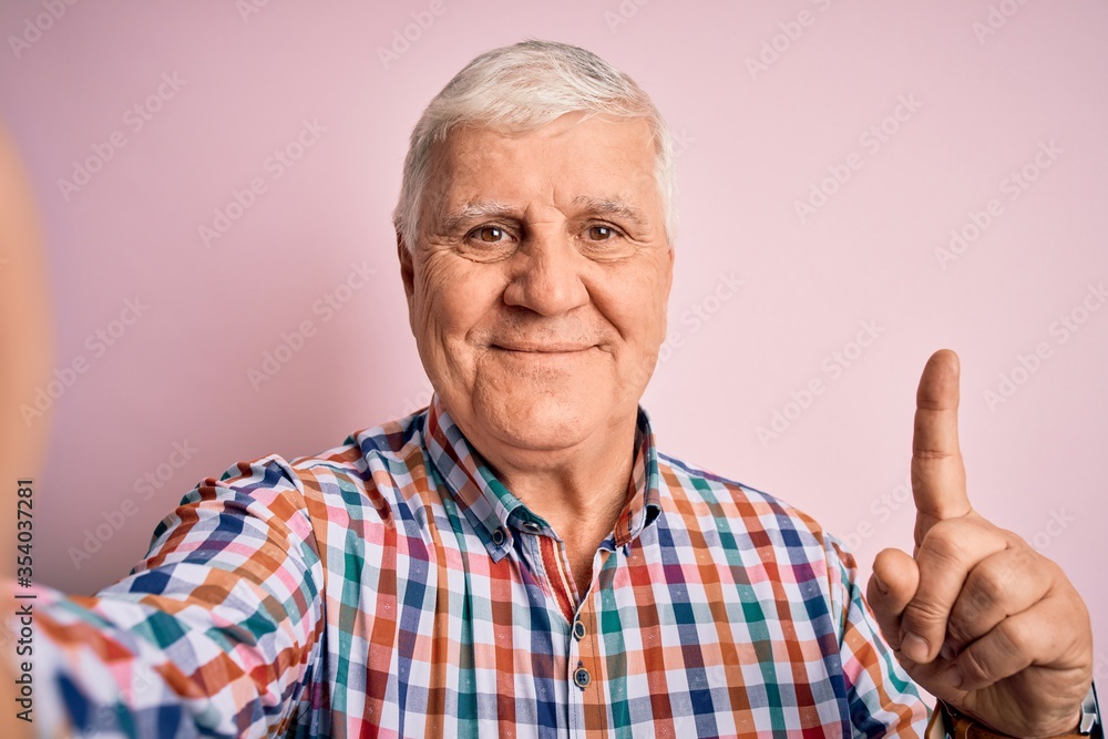Senior handsome hoary man wearing casual shirt making selfie by the camera surprised with an idea or question pointing finger with happy face, number one Senior handsome hoary man wearing casual shirt making selfie by the camera surprised with an idea or question pointing finger with happy face, number one