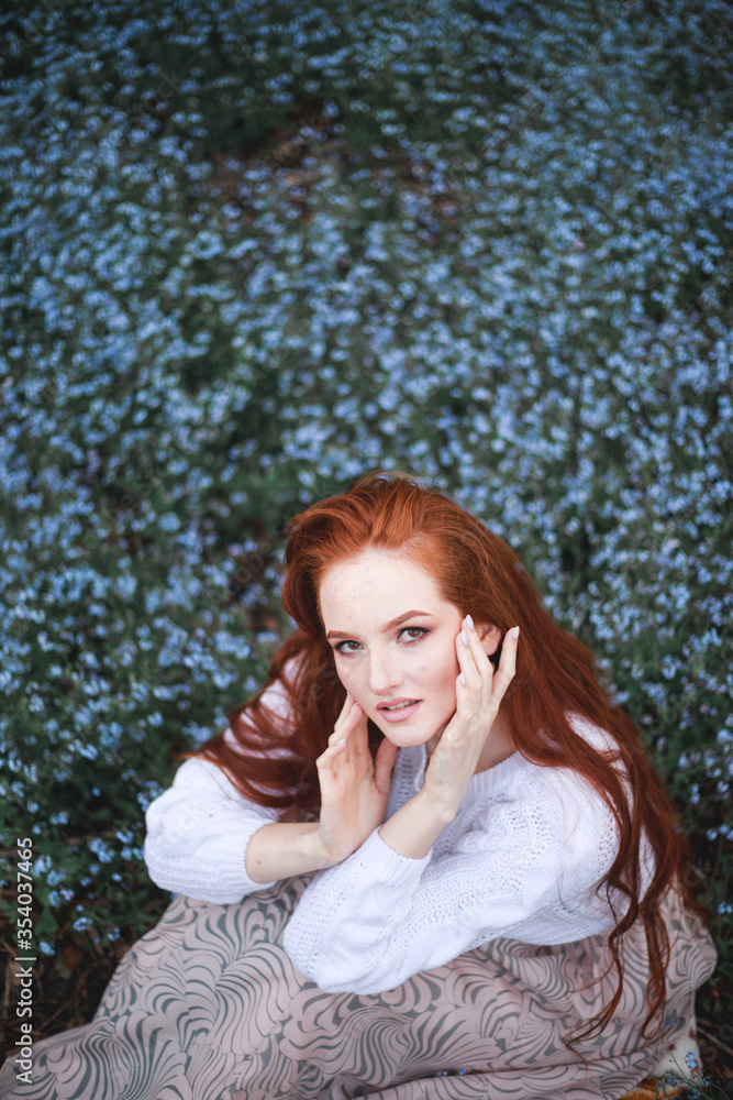 a girl in a white sweater sits in a clearing among forget me nots