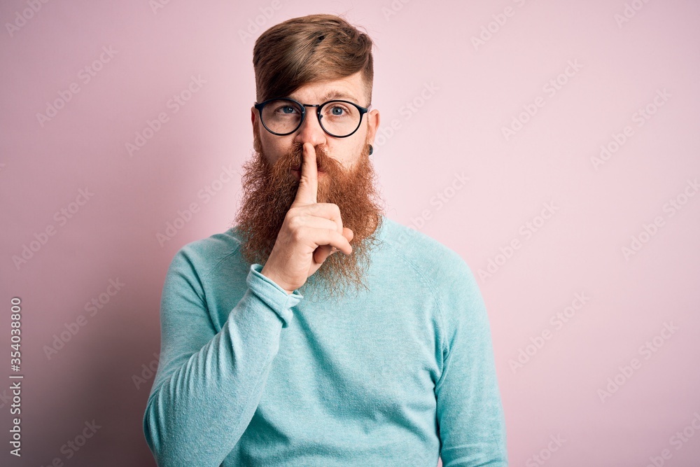 Handsome Irish redhead man with beard wearing glasses over pink isolated background asking to be quiet with finger on lips. Silence and secret concept.