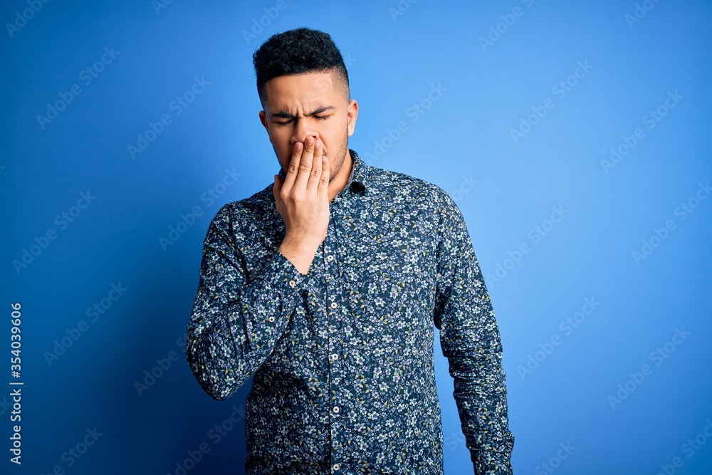 Young handsome man wearing casual shirt standing over isolated blue background bored yawning tired covering mouth with hand. Restless and sleepiness. Young handsome man wearing casual shirt standing over isolated blue background bored yawning tired covering mouth with hand. Restless and sleepiness.