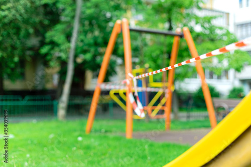 Children's playground on the grass in the park wrapped with red barrier tape. Prohibition of outdoor walks, prevention of the biological hazard of the influenza virus covid-19. selective focus