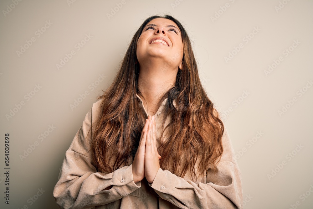 Φωτογραφία Young beautiful brunette woman wearing casual shirt standing over white background begging and praying with hands together with hope expression on face very emotional and worried