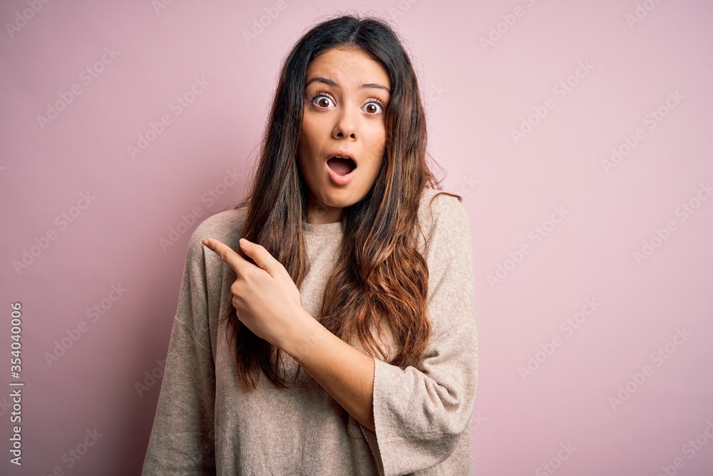 Young beautiful brunette woman wearing casual sweater standing over pink background Surprised pointing with finger to the side, open mouth amazed expression. Young beautiful brunette woman wearing casual sweater standing over pink background Surprised pointing with finger to the side, open mouth amazed expression.