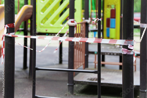 The play park for young children is wrapped in red barrier tape. Outside. Prohibition of outdoor walks, prevention of the coronavirus influenza virus covid-19. city street. selective focus