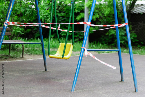 Yellow children's swing on a sports playground wrapped with red barrier tape. Outside. Prohibition of outdoor walks, prevention of the coronavirus influenza virus covid-19. barred. selective focus