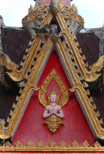 Pediment design showing a buddha image on red background in a wat or buddhist temple in Siamese Lao PDR, Southeast Asia
