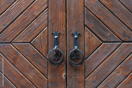 Vintage brown wooden door with two forged handles close up.