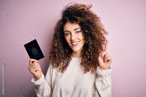 Beautiful tourist woman with curly hair and piercing holding canada canadian passport id surprised with an idea or question pointing finger with happy face, number one
