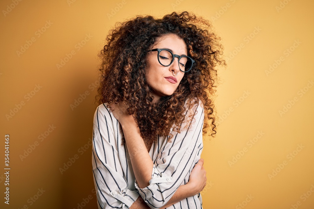 Young beautiful woman with curly hair and piercing wearing striped shirt and glasses Hugging oneself happy and positive, smiling confident. Self love and self care Young beautiful woman with curly hair and piercing wearing striped shirt and glasses Hugging oneself happy and positive, smiling confident. Self love and self care