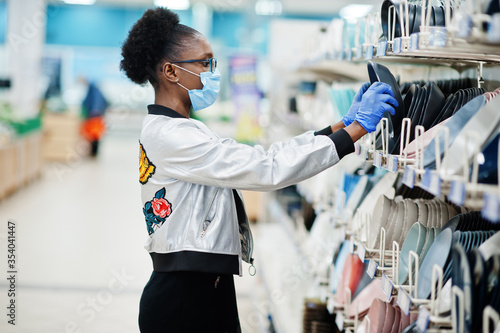 African woman wearing disposable medical mask and gloves shopping in supermarket during coronavirus pandemia outbreak. Black female choose bowl at epidemic time.