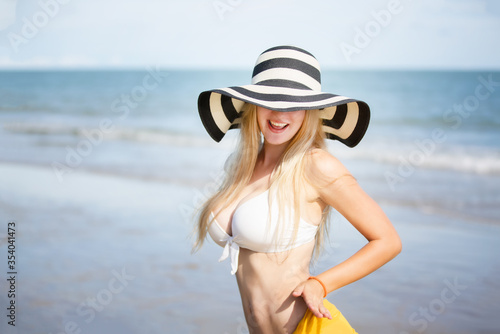Happy woman smiling and having fun at beach. Summer portrait of young beautiful girl running on beach with a hat. girl laughing and looking at camera with joy.