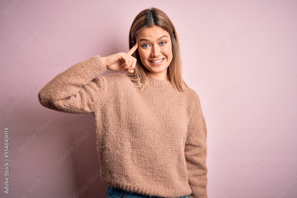 Young beautiful blonde woman wearing winter wool sweater over pink isolated background Smiling pointing to head with one finger, great idea or thought, good memory Young beautiful blonde woman wearing winter wool sweater over pink isolated background Smiling pointing to head with one finger, great idea or thought, good memory