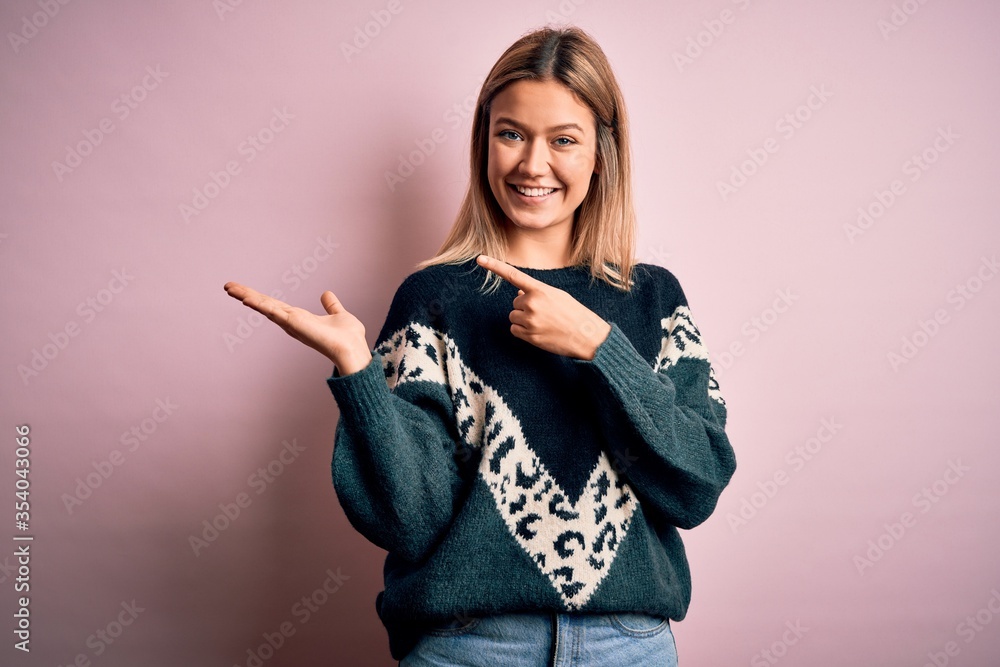 Young beautiful blonde woman wearing fashion sweater over pink isolated background amazed and smiling to the camera while presenting with hand and pointing with finger. Young beautiful blonde woman wearing fashion sweater over pink isolated background amazed and smiling to the camera while presenting with hand and pointing with finger.