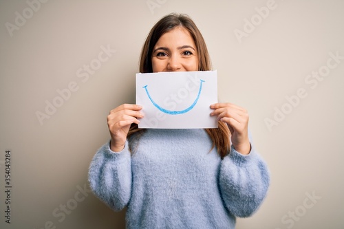 Young blonde woman holding funny smile drawing on mouth as happy expression with a happy face standing and smiling with a confident smile showing teeth