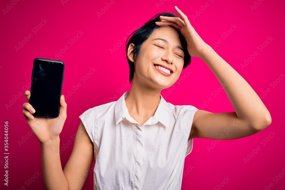 Young beautiful asian girl holding smartphone showing screen over isolated pink background stressed with hand on head, shocked with shame and surprise face, angry and frustrated. Fear and upset Young beautiful asian girl holding smartphone showing screen over isolated pink background stressed with hand on head, shocked with shame and surprise face, angry and frustrated. Fear and upset