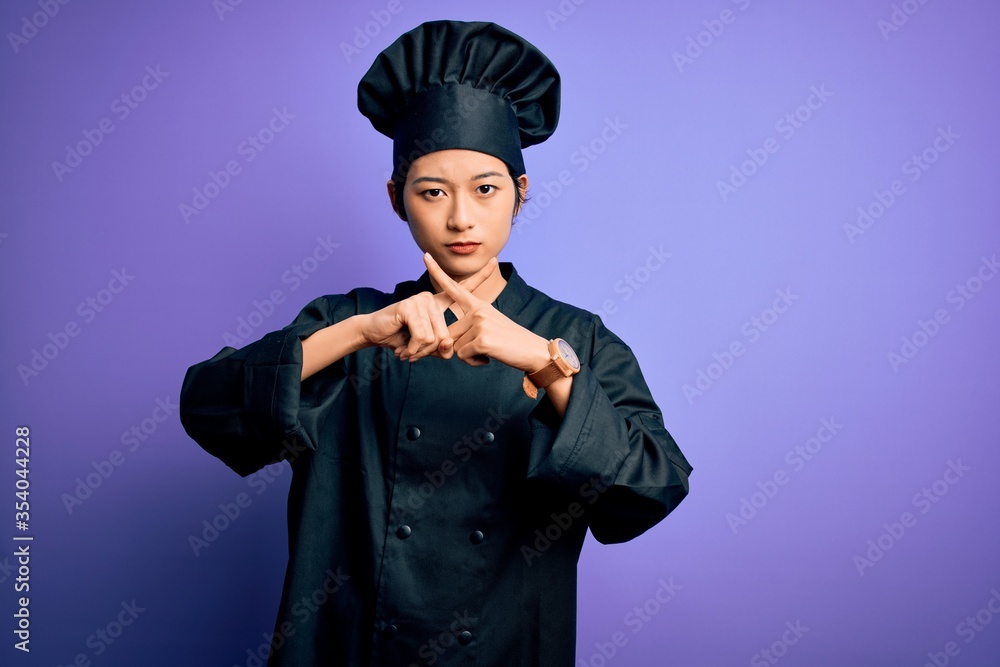 Young beautiful chinese chef woman wearing cooker uniform and hat over purple background Rejection expression crossing fingers doing negative sign Young beautiful chinese chef woman wearing cooker uniform and hat over purple background Rejection expression crossing fingers doing negative sign