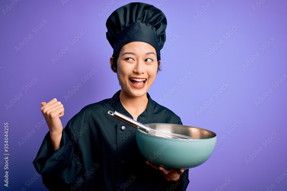 Young beautiful chinese chef woman wearing cooker uniform and hat using bowl and whisk pointing and showing with thumb up to the side with happy face smiling Young beautiful chinese chef woman wearing cooker uniform and hat using bowl and whisk pointing and showing with thumb up to the side with happy face smiling