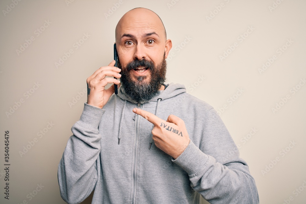 Obraz premium Handsome bald man with beard having conversation talking on the smartphone very happy pointing with hand and finger