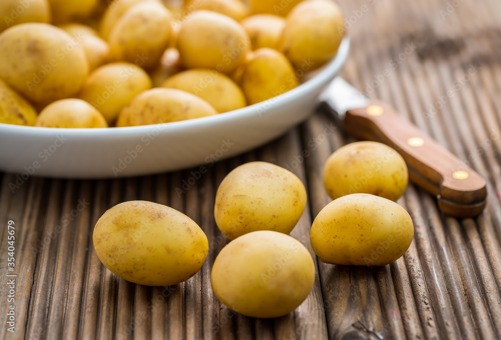 Fresh organic small potatoes in bowl with knife on wooden background Fresh organic small potatoes in bowl with knife on wooden background