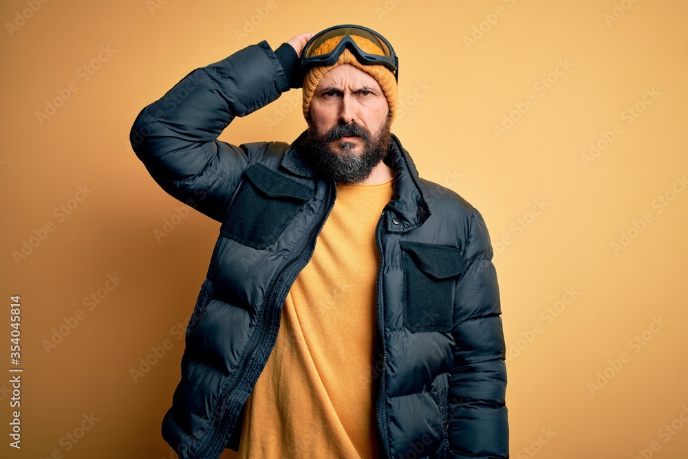 Handsome skier bald man with beard skiing wearing snow sportswear and ski goggles confuse and wonder about question. Uncertain with doubt, thinking with hand on head. Pensive concept. Handsome skier bald man with beard skiing wearing snow sportswear and ski goggles confuse and wonder about question. Uncertain with doubt, thinking with hand on head. Pensive concept.