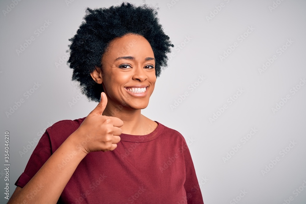 Young beautiful African American afro woman with curly hair wearing casual t-shirt standing doing happy thumbs up gesture with hand. Approving expression looking at the camera showing success. Young beautiful African American afro woman with curly hair wearing casual t-shirt standing doing happy thumbs up gesture with hand. Approving expression looking at the camera showing success.