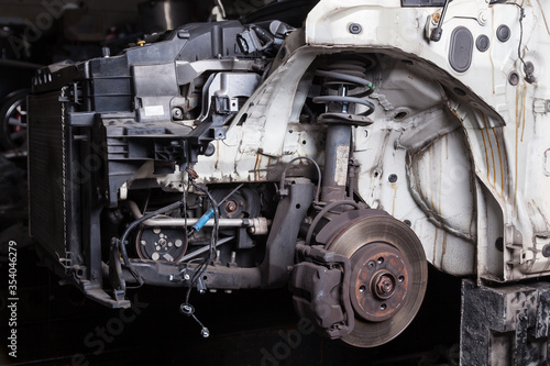 The front of the car after an accident with a disassembled body and metal elements and assemblies under the hood in a car repair shop or garage against a dark background.