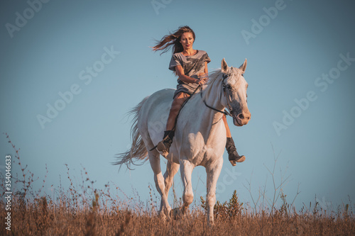 Woman walking and riding with her white horse on the fields during sunset