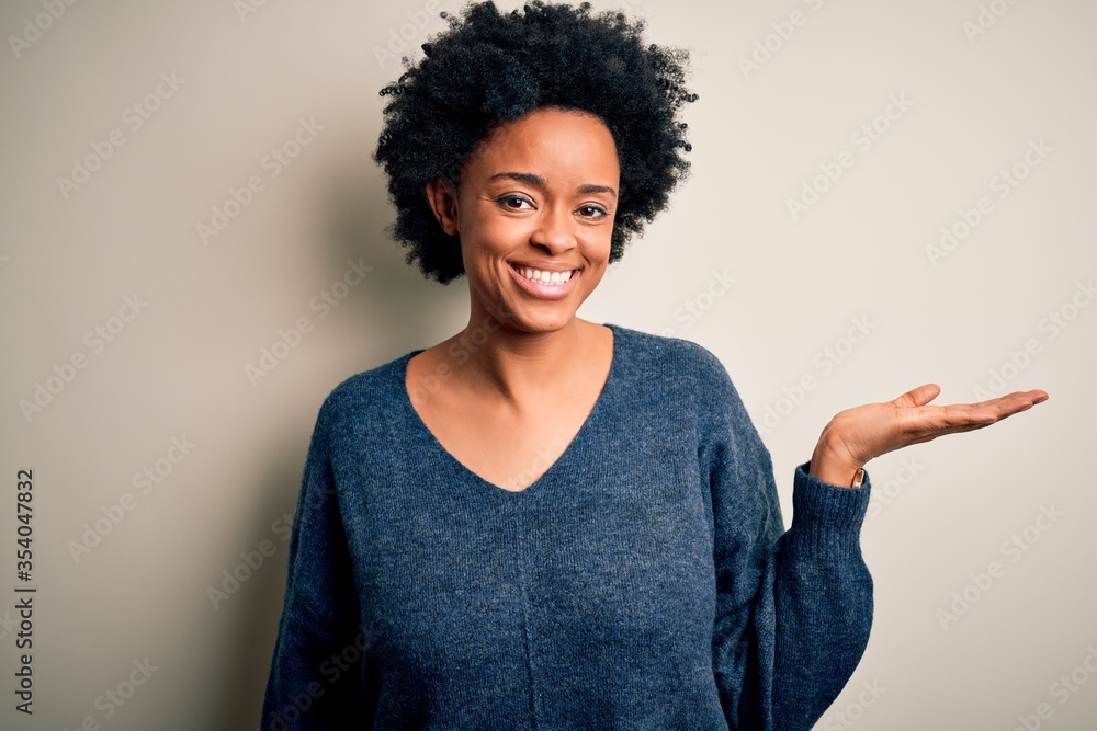 Young beautiful African American afro woman with curly hair wearing casual sweater smiling cheerful presenting and pointing with palm of hand looking at the camera. Young beautiful African American afro woman with curly hair wearing casual sweater smiling cheerful presenting and pointing with palm of hand looking at the camera.