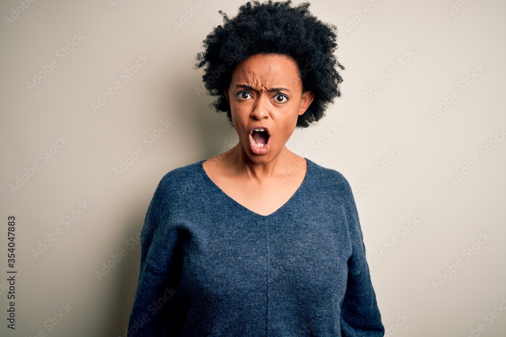 Young beautiful African American afro woman with curly hair wearing casual sweater In shock face, looking skeptical and sarcastic, surprised with open mouth Young beautiful African American afro woman with curly hair wearing casual sweater In shock face, looking skeptical and sarcastic, surprised with open mouth