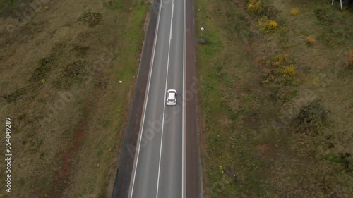 Aerial view of a white car riding along the highway through the flat fields. Drone follows the car on the road in 4k.