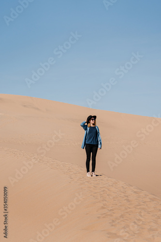 A travel girl is standing in the middle of a sand dune. A traveler in a black hat and blue skirt in Death Valley National Park