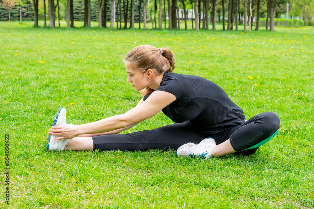 beautiful girl warming up before doing sports sitting on grass in park beautiful girl warming up before doing sports sitting on grass in park