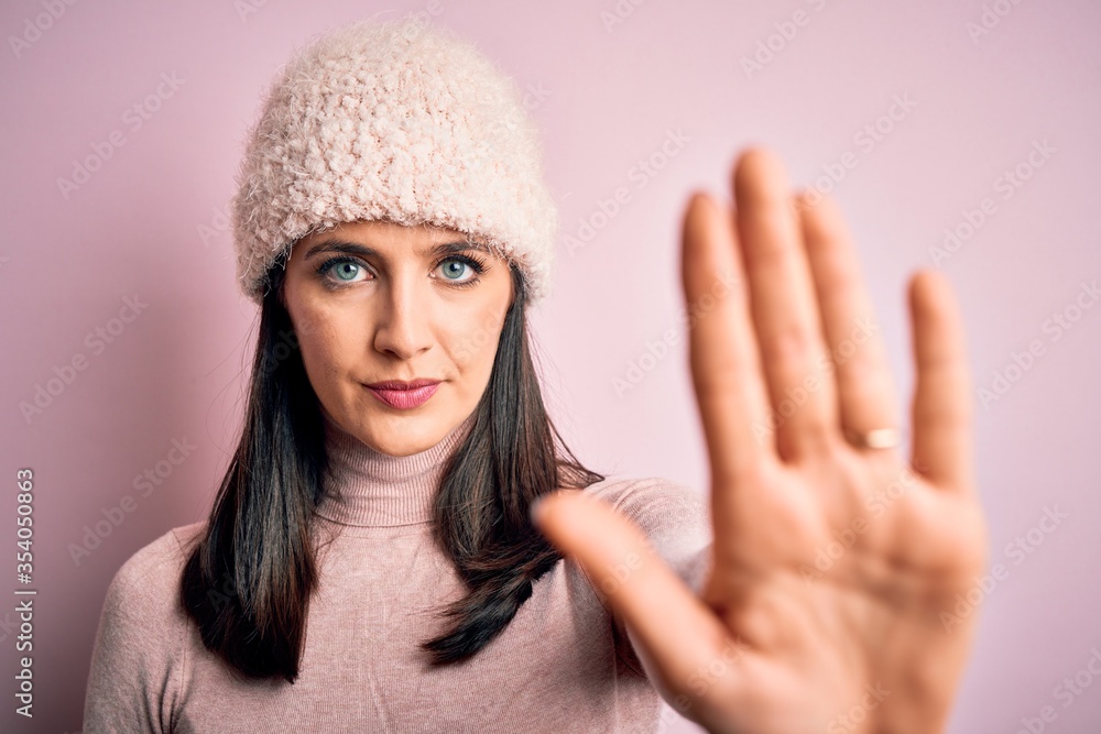 Young brunette woman with blue eyes wearing casual t-shirt and wool cap standing with open hand doing stop sign with serious and confident expression, defense gesture Young brunette woman with blue eyes wearing casual t-shirt and wool cap standing with open hand doing stop sign with serious and confident expression, defense gesture