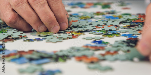 elderly person with wrinkled hands does colorful puzzles at light table