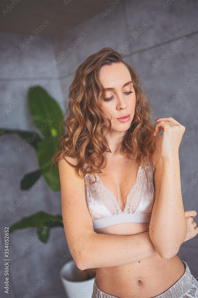 Winsome slim fit long-curly-haired woman in cozy velvet beige lingerie homewear posing beside big domestic green palm tree plant. Indoor unretouched portrait of gorgeous young natural beauty lady Winsome slim fit long-curly-haired woman in cozy velvet beige lingerie homewear posing beside big domestic green palm tree plant. Indoor unretouched portrait of gorgeous young natural beauty lady