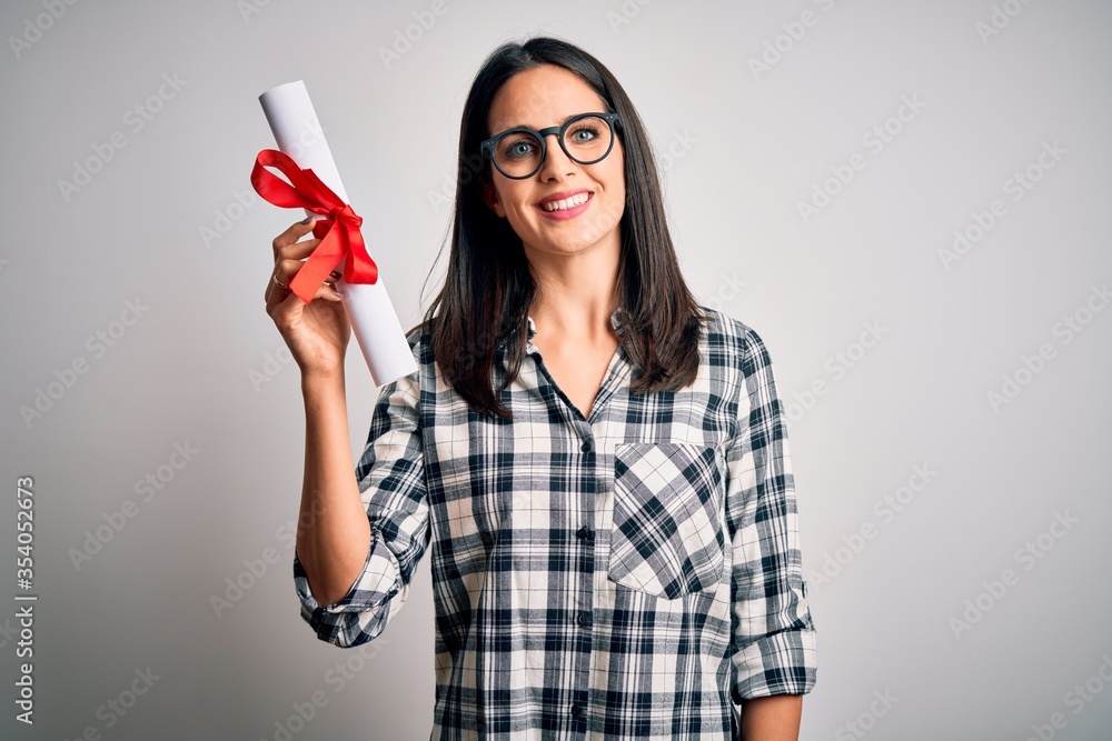 Young brunette student woman with blue eyes holding university diploma over isolated background with a happy face standing and smiling with a confident smile showing teeth Young brunette student woman with blue eyes holding university diploma over isolated background with a happy face standing and smiling with a confident smile showing teeth