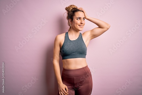 Young beautiful blonde sportswoman doing sport wearing sportswear over pink background smiling confident touching hair with hand up gesture, posing attractive and fashionable