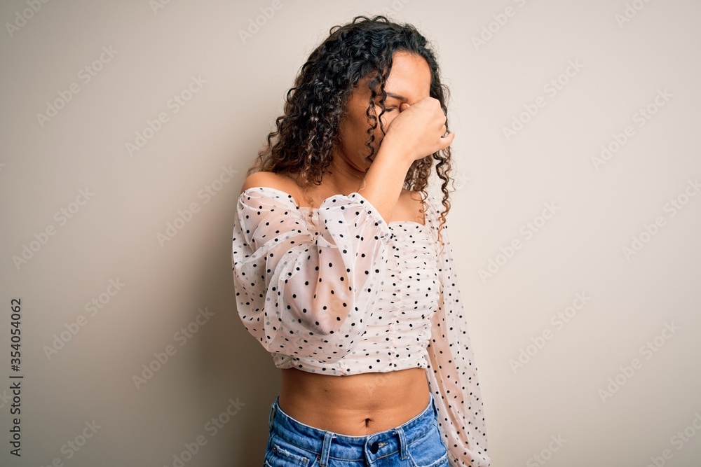 Young beautiful woman with curly hair wearing casual t-shirt standing over white background tired rubbing nose and eyes feeling fatigue and headache. Stress and frustration concept. Young beautiful woman with curly hair wearing casual t-shirt standing over white background tired rubbing nose and eyes feeling fatigue and headache. Stress and frustration concept.