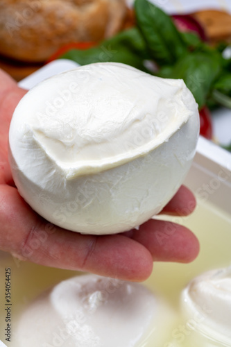 Cheese maker holding in hand fresh handmade soft Italian cheese from Campania, white balls of buffalo mozzarella cheese made from cow milk in container with water