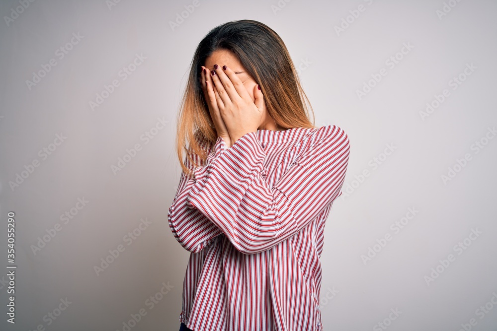 Young beautiful blonde woman with blue eyes wearing stiped t-shirt over white background with sad expression covering face with hands while crying. Depression concept. Young beautiful blonde woman with blue eyes wearing stiped t-shirt over white background with sad expression covering face with hands while crying. Depression concept.